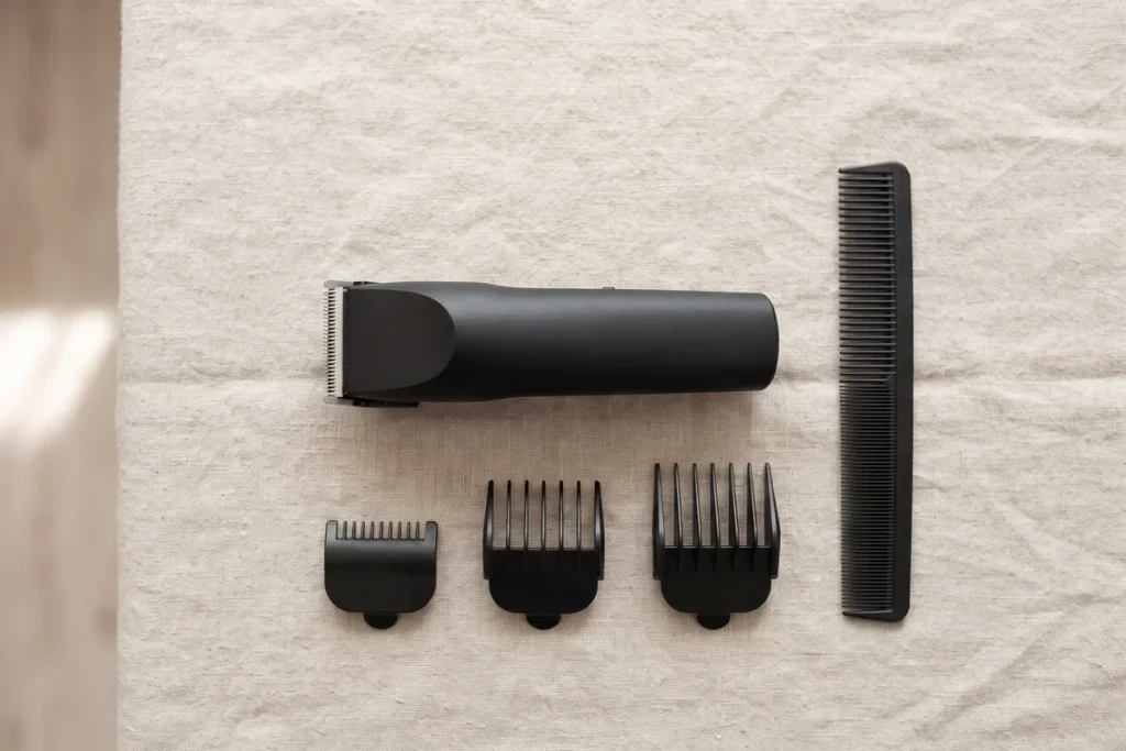 A black hair clipper, three clipper guards of different lengths and a black comb on linen