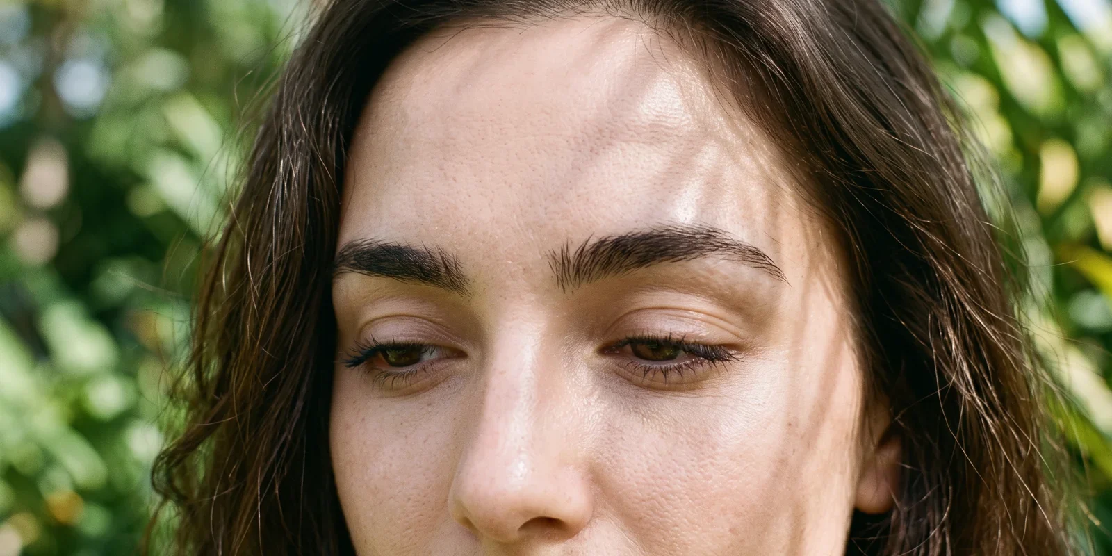 Close-up of a woman's face with natural, softly defined dark brown eyebrows in soft outdoor light