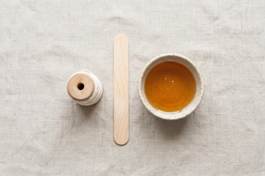 A spool of cotton thread, a clean wooden spatula and a small bowl of warm wax on a linen towel
